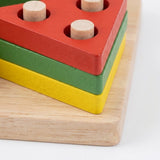 A wooden stacking toy with three colored layers: red on top, green in the middle, and yellow on the bottom, each with a natural wood peg inserted into the top slot, shown on a light wood base against a white background.