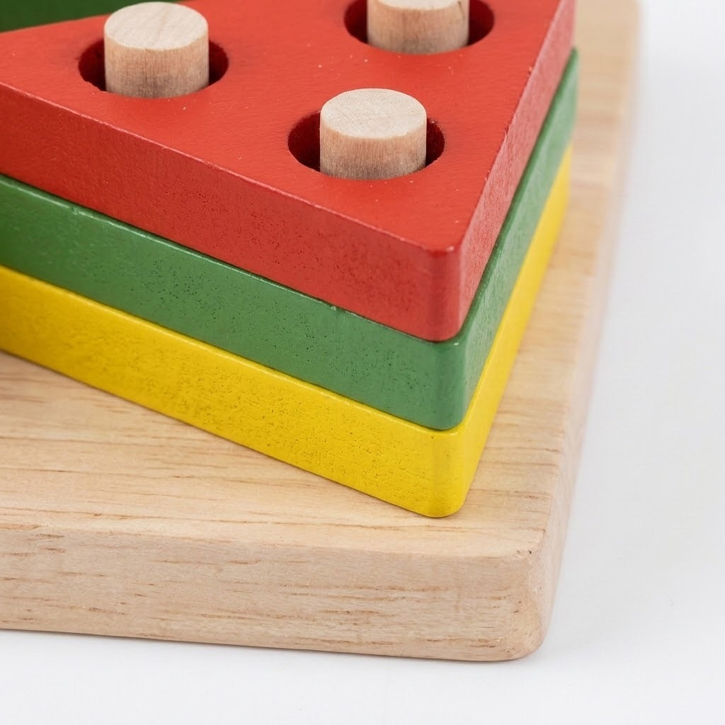 A wooden stacking toy with three colored layers: red on top, green in the middle, and yellow on the bottom, each with a natural wood peg inserted into the top slot, shown on a light wood base against a white background.