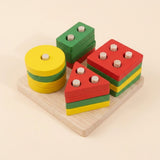 Wooden Montessori shape-sorting blocks on a light wood base, featuring yellow and green circular discs and red, green, and yellow triangular and square blocks with small silver pegs.
