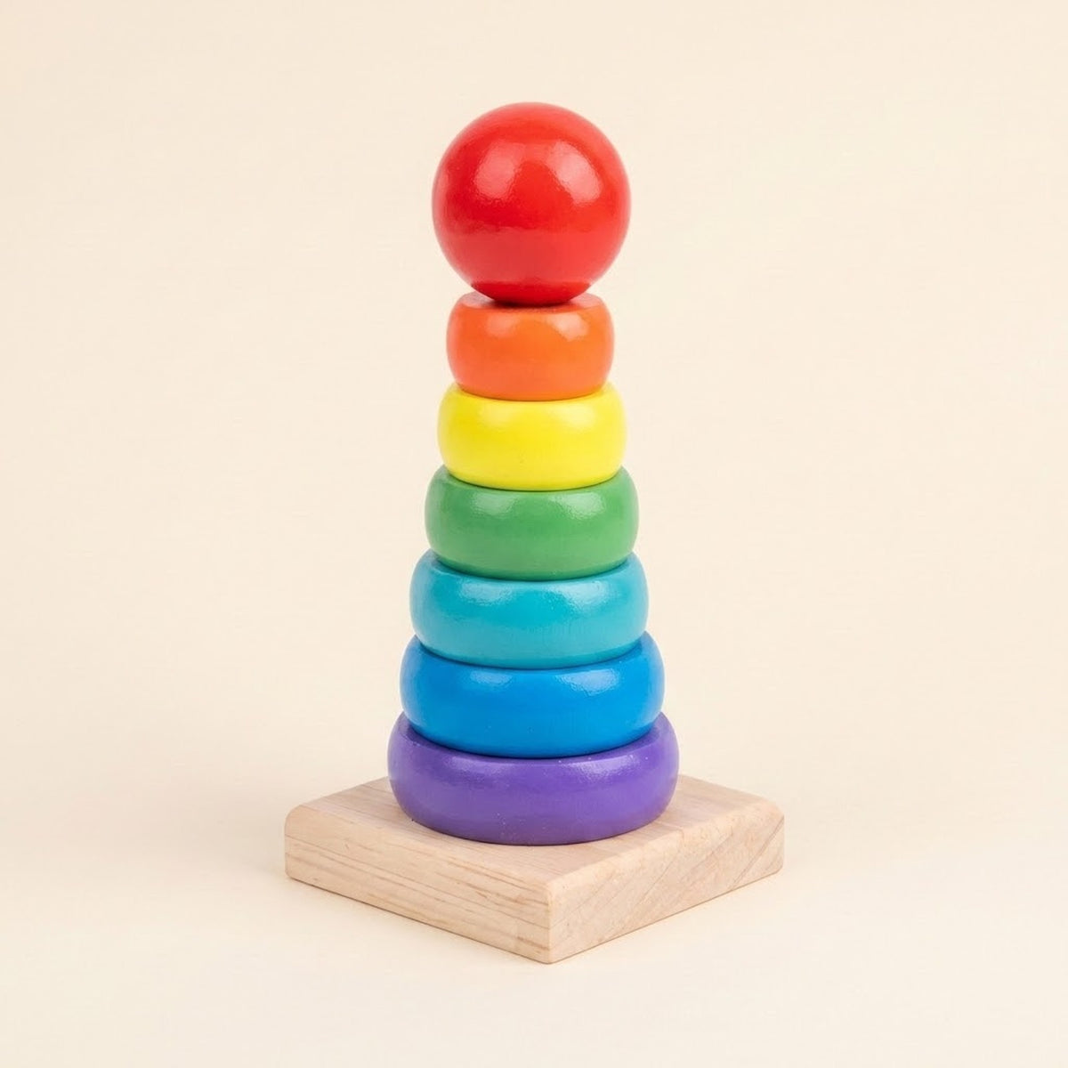 Wooden educational toy with rainbow stacking rings and a red ball on a square natural wood base against a beige background.