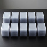 Ten stacks of clear plastic card sleeves or protective cases arranged in two rows on a dark surface against a gray background.