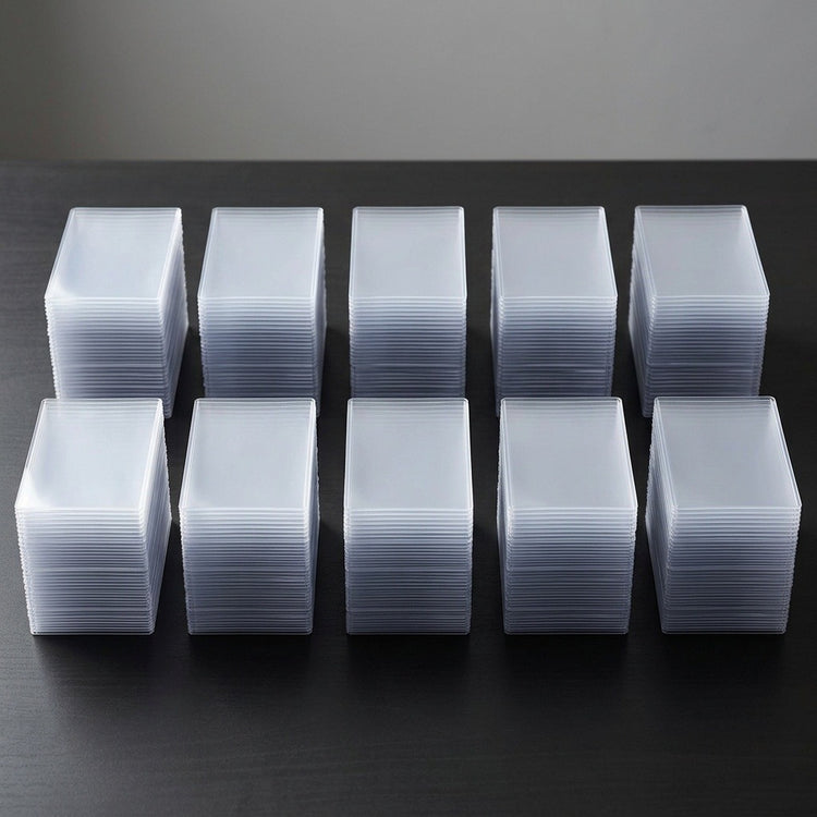 Ten stacks of clear plastic card sleeves or protective cases arranged in two rows on a dark surface against a gray background.
