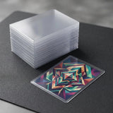 A stack of clear plastic card sleeves sits on a dark textured surface next to a single card sleeve containing a colorful geometric patterned card.
