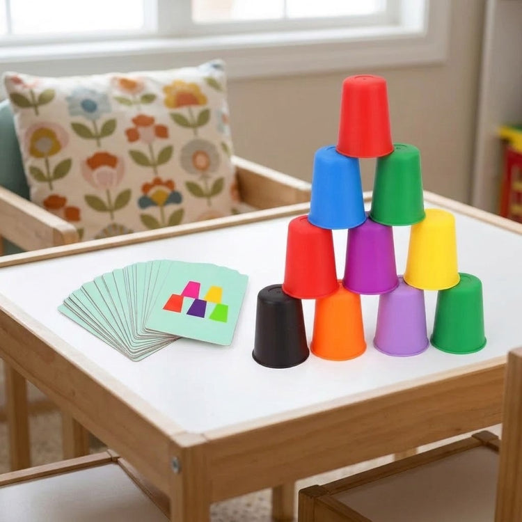 Cup stacking game with colorful plastic cups arranged in a pyramid beside fanned pattern cards on a white-topped wooden table.