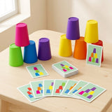 A colorful children's stacking card game set arranged on a light wood table near a window. The set includes multiple plastic cups in bright colors (pink, blue, purple, green, yellow, orange, red) and matching geometric instruction cards.
