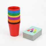 Cup stacking game with multicolored plastic cups nested together beside a neatly stacked deck of pattern cards on white.
