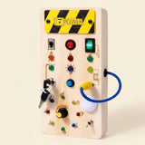 Pale wooden busy board with musical symbols, colorful lights, switches, keys, and a blue looped cord stands against a cream background.