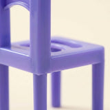A purple plastic chair piece from the stacking game shows seat openings, backrest details and slender legs against a cream background.