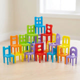 Chair stacking game with multicoloured plastic pieces arranged in a stepped pyramid on a pale wooden table beneath a bright window.