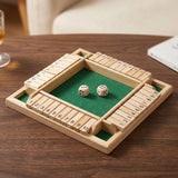 A natural wood four-player shut the box game with green felt and two wooden dice on a dark wooden table.