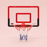 Basketball hoop with a red and black backboard, red rim and red, white and blue net appears against a pale pink background.