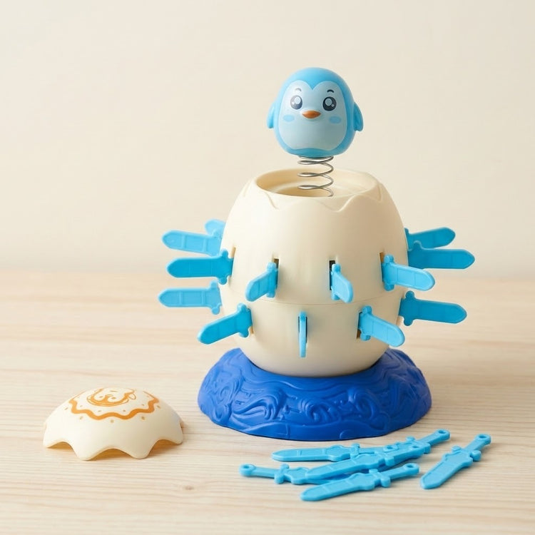 Penguin tabletop game shows a blue penguin raised on a spring above a cream barrel, with loose swords on a pale wooden table.