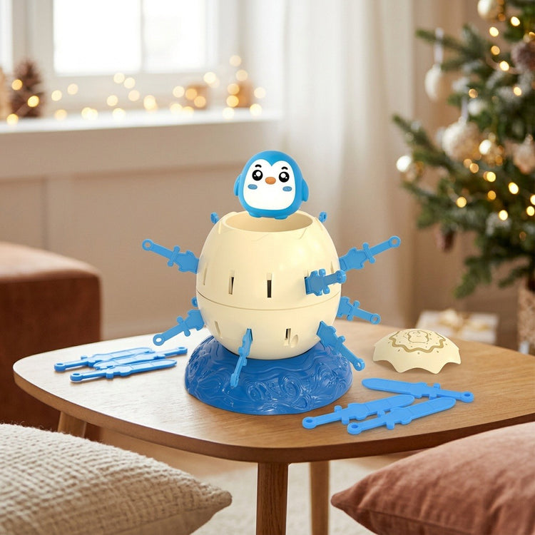 Penguin tabletop game with a cream barrel, blue swords and detached lid sits on a wooden table beside a decorated Christmas tree.