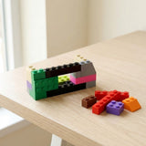 Multicolored plastic building blocks form an open rectangular structure beside loose pieces on a pale wooden table near a window.