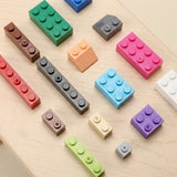 Colorful plastic building blocks with round studs, rectangular shapes, and a sloped piece lie separately on a pale wooden tabletop.