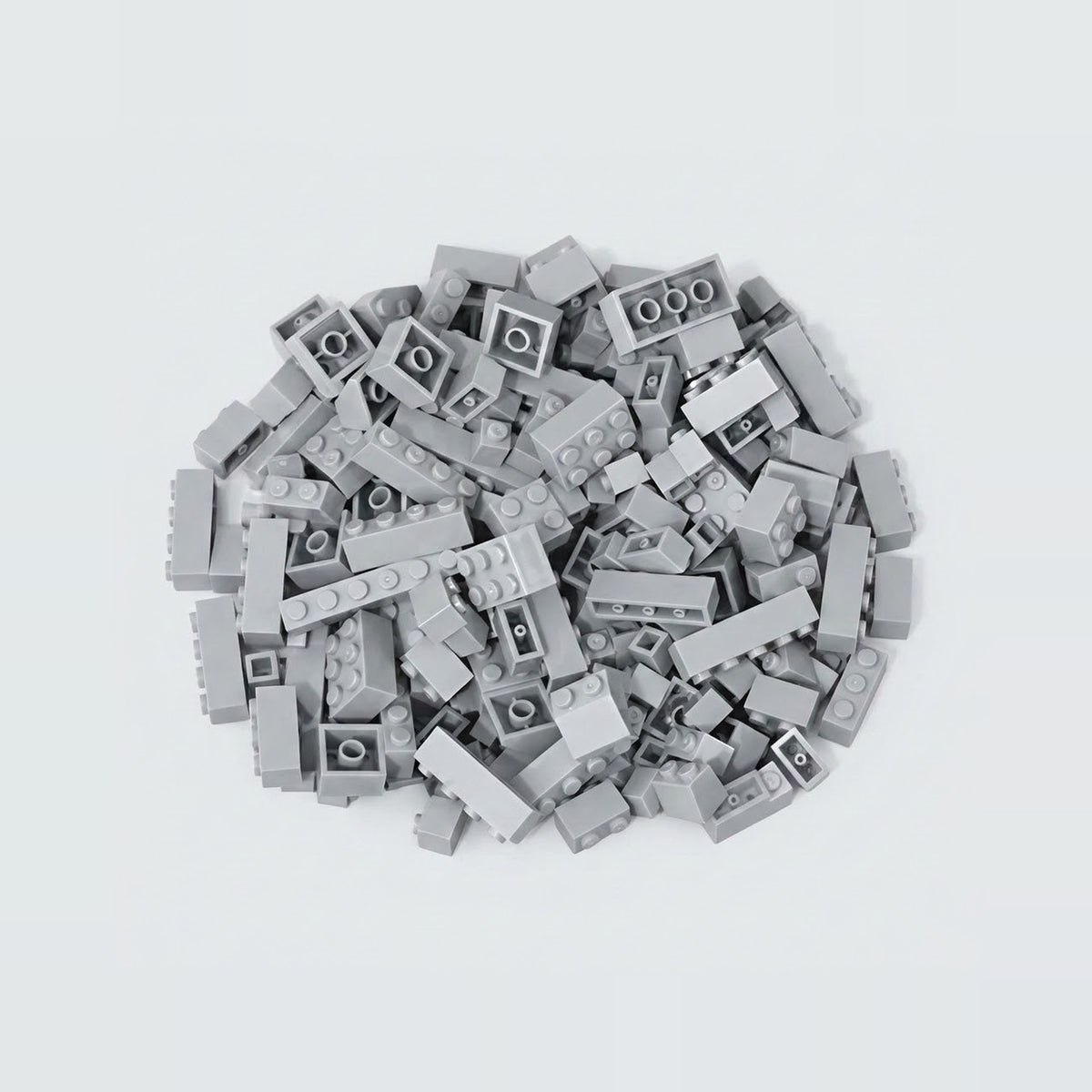 A compact pile of light gray building bricks rests on a pale background, with square and rectangular pieces facing different directions.