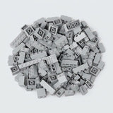 Light gray building bricks form a broad pile on a pale background, displaying round studs, smooth sides, and hollow undersides.