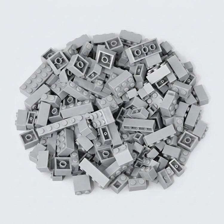 Light gray building bricks form a broad pile on a pale background, displaying round studs, smooth sides, and hollow undersides.