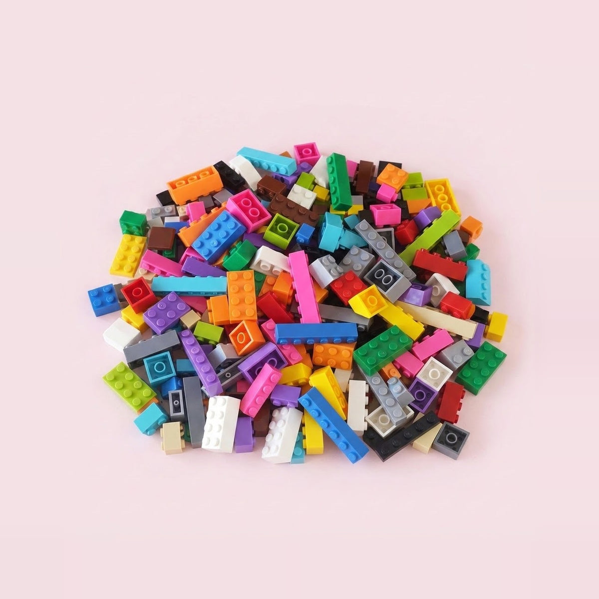 Multicolored building bricks in assorted shapes form a compact pile on a pale pink background.