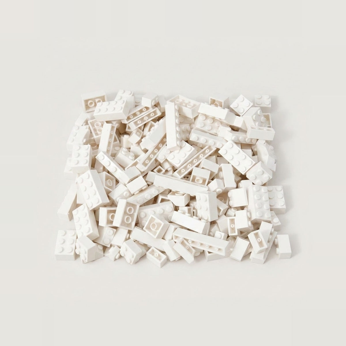 White building bricks in assorted square and rectangular shapes form a compact pile on an off-white background.