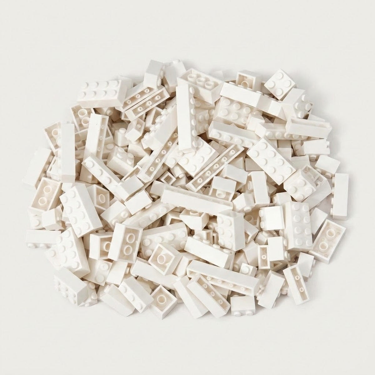 A broad pile of white building bricks rests on an off-white background, with round studs and hollow undersides visible.