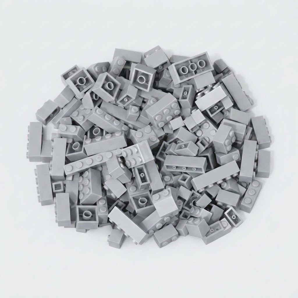 Light gray building bricks in assorted shapes form a loose pile on a white background, showing studs and hollow undersides.