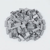 Light gray building bricks in assorted shapes form a loose pile on a white background, showing studs and hollow undersides.