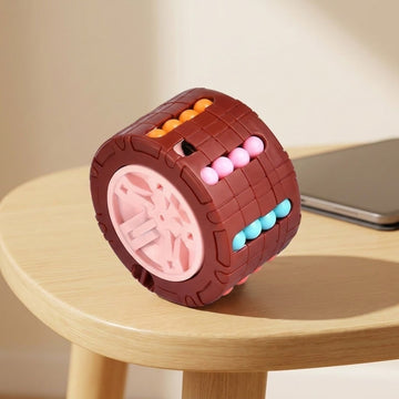Brown cylinder fidget puzzle with a pink wheel end and colorful beads on a round wooden table beside a closed laptop.