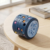 Blue cylinder fidget puzzle with scattered colorful beads on a round wooden table near a book and sunlit window.