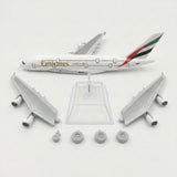 White model airplane fuselage, detached silver wings with engines, four landing gear pieces, and clear display stand arranged on white.