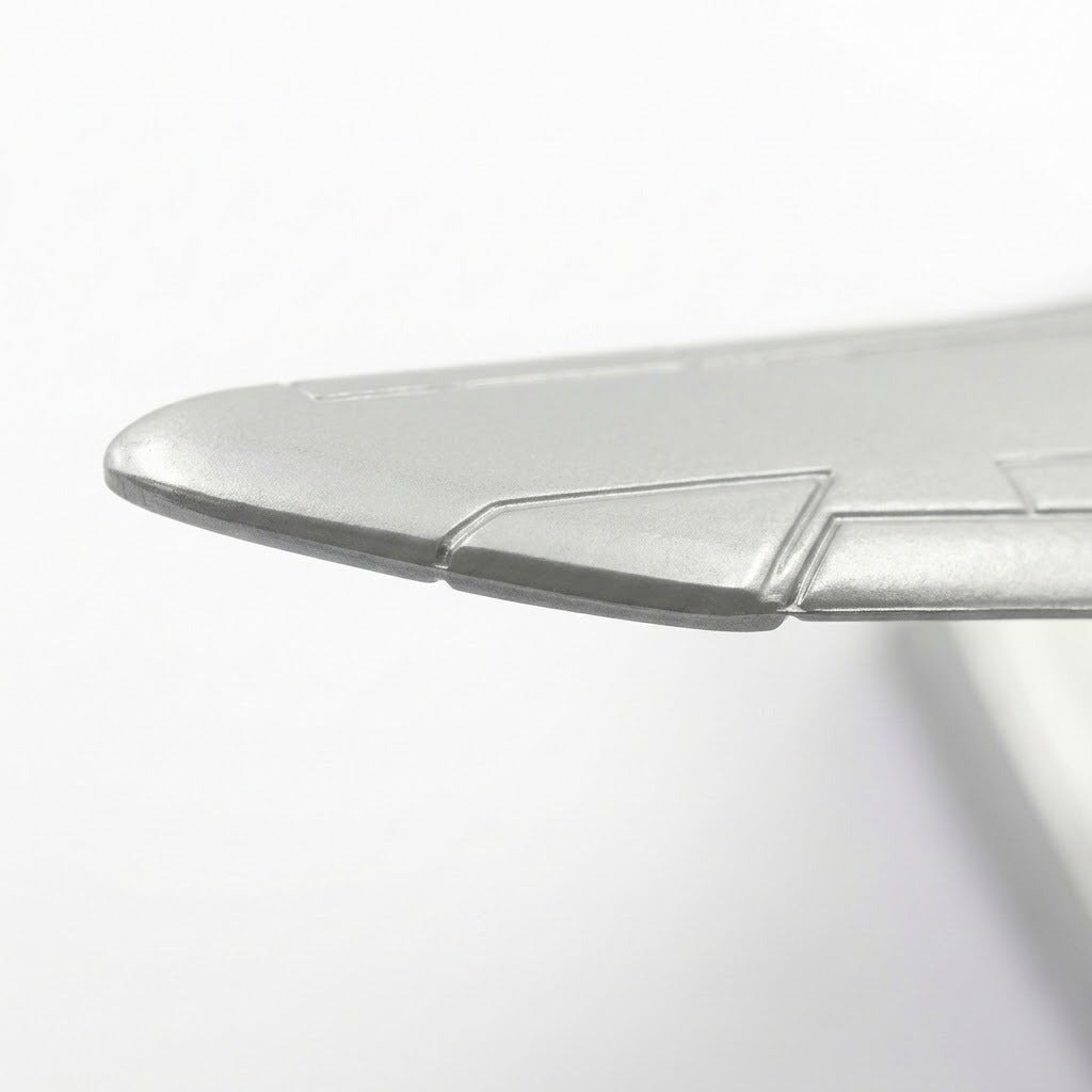 Close-up of a silver model airplane wing showing its metallic edge and engraved panel details against white.