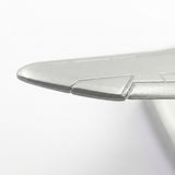 Close-up of a silver model airplane wing showing its metallic edge and engraved panel details against white.