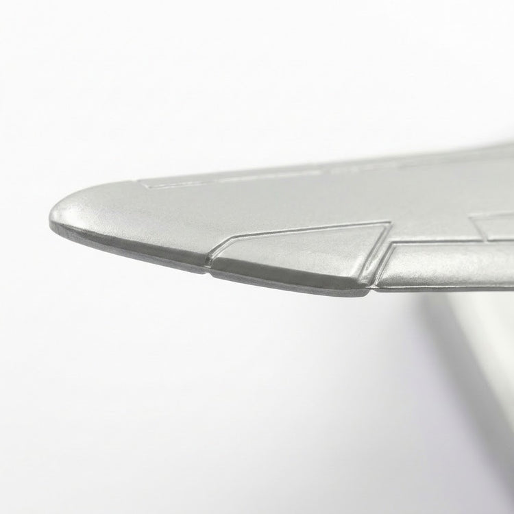 Close-up of a silver model airplane wing showing its metallic edge and engraved panel details against white.