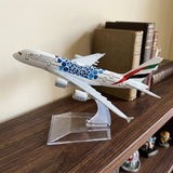White model airplane with blue circular patterns on a clear stand on a dark wooden shelf beside books.