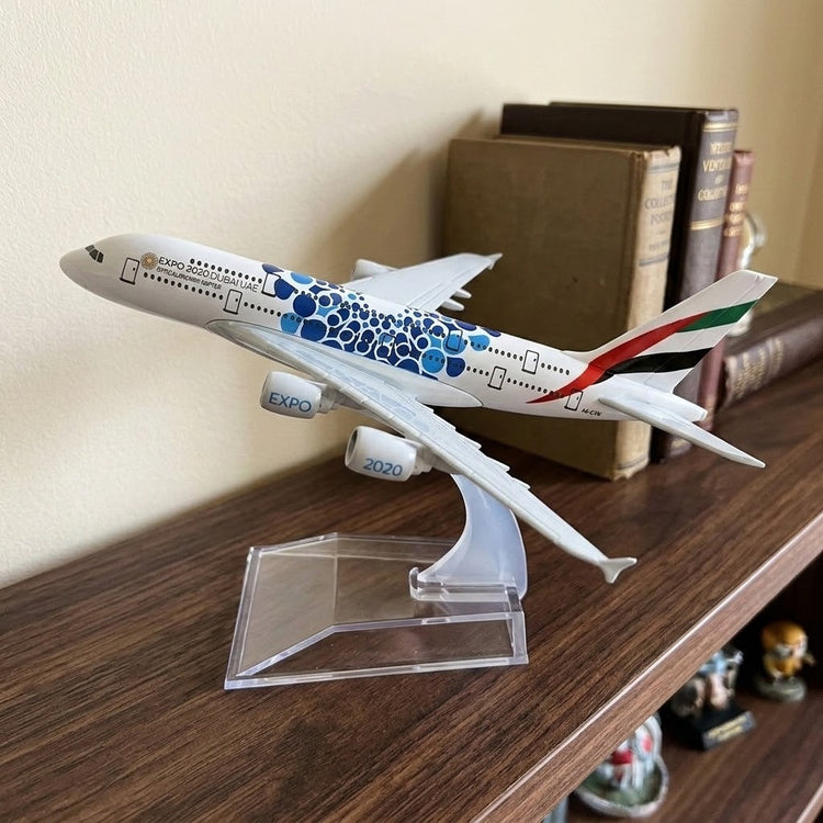 White model airplane with blue circular patterns on a clear stand on a dark wooden shelf beside books.