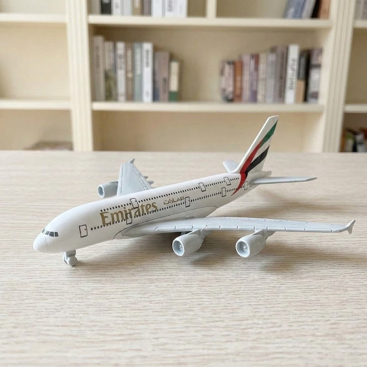 White model airplane resting on landing wheels on a pale wooden tabletop with bookshelves in the background.