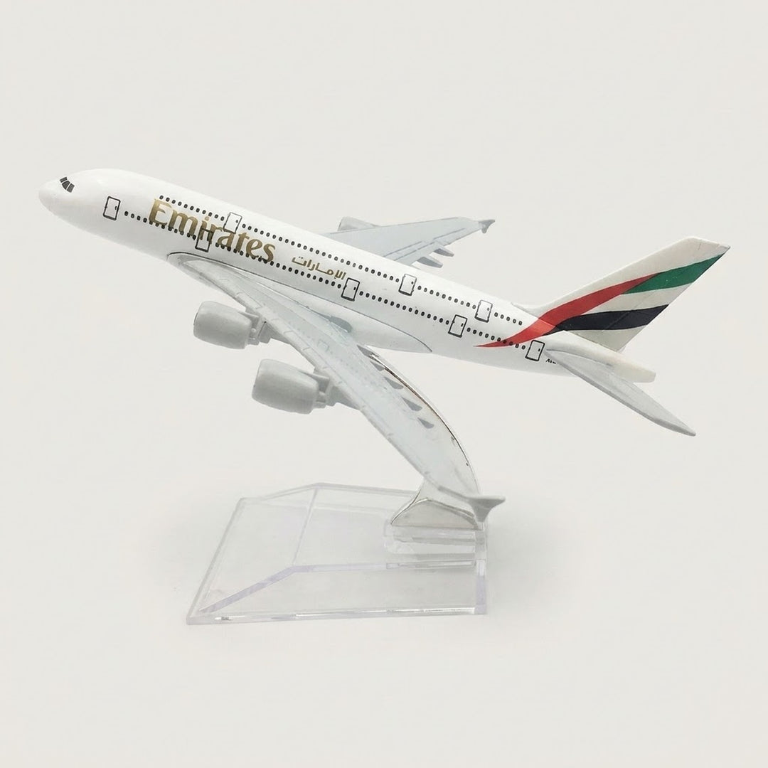 White four-engine model airplane with red, green, and black tail stripes, angled upward on a transparent display stand against a white background.