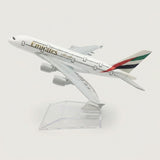 White four-engine model airplane with red, green, and black tail stripes, angled upward on a transparent display stand against a white background.