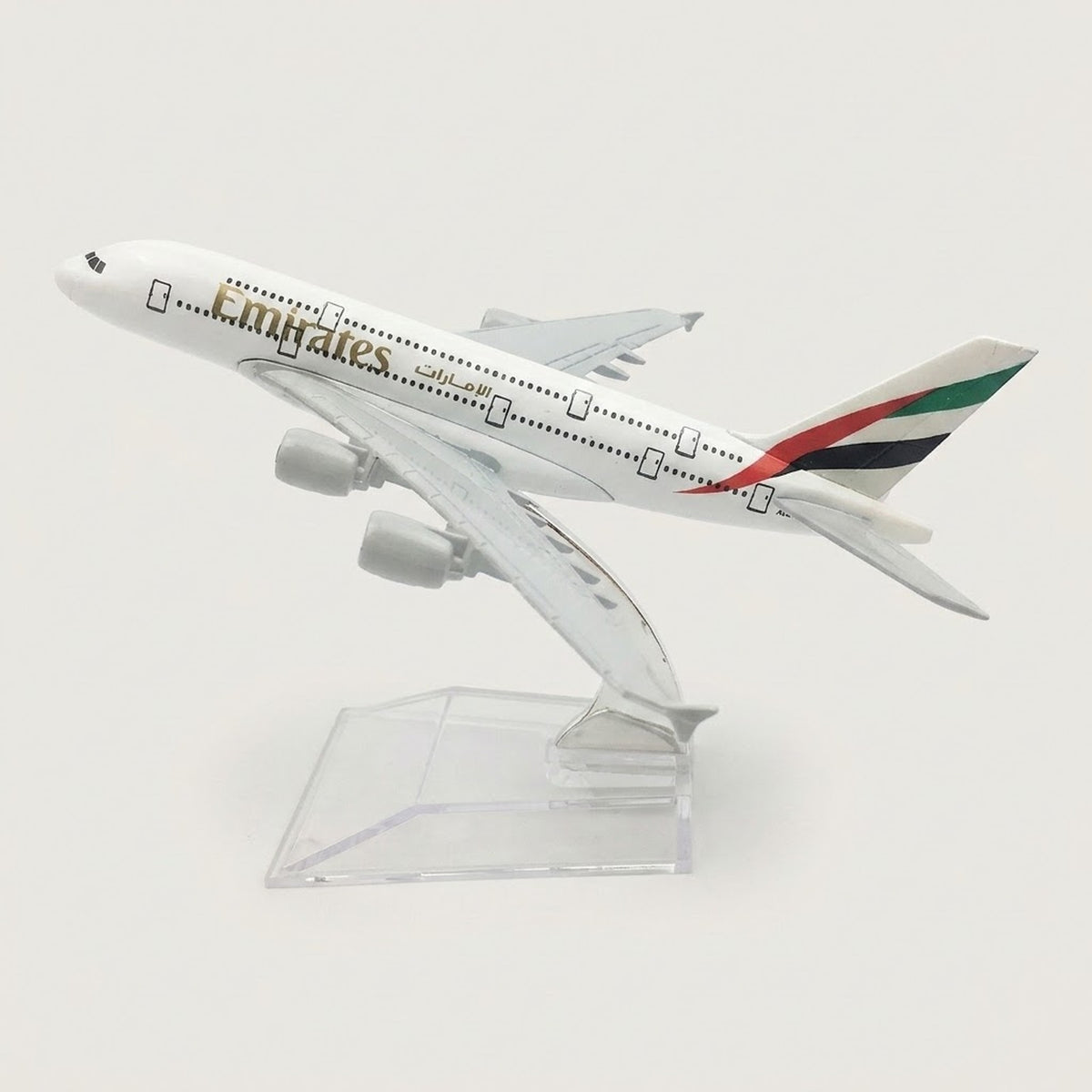 White four-engine model airplane with red, green, and black tail stripes, angled upward on a transparent display stand against a white background.