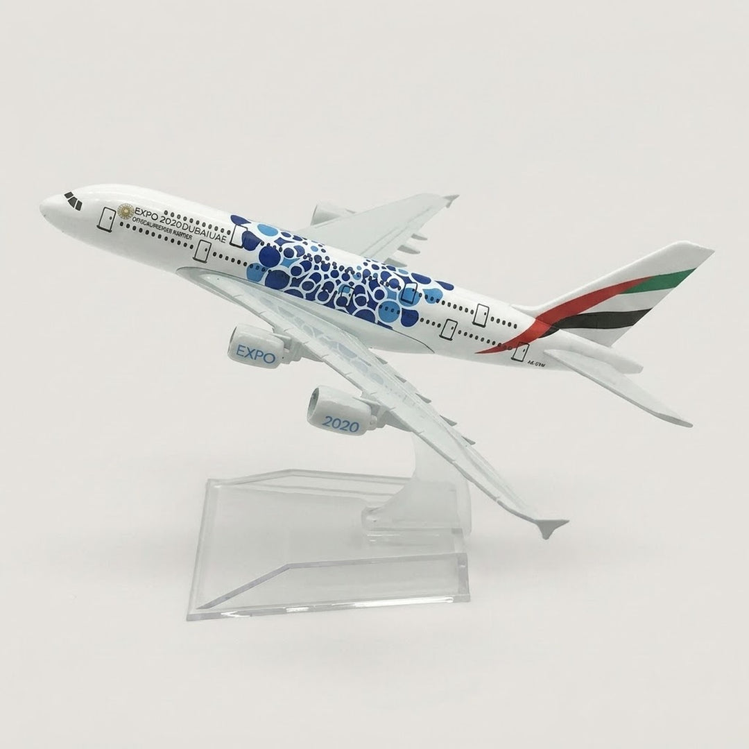 White model airplane with blue circular patterns and a striped tail, angled upward on a transparent display stand against a white background.