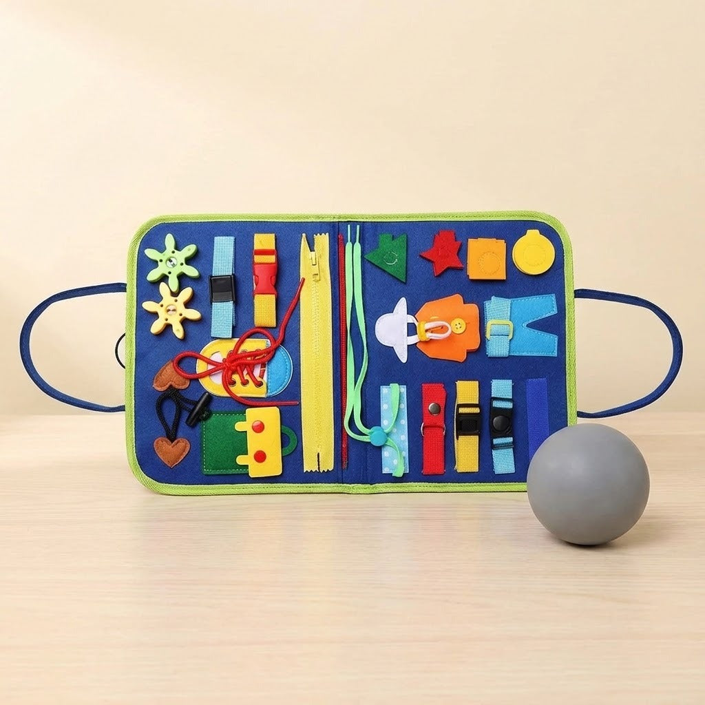 An open blue busy board with green trim, colourful buckles, zippers and laces stands on a wooden surface beside a grey ball.