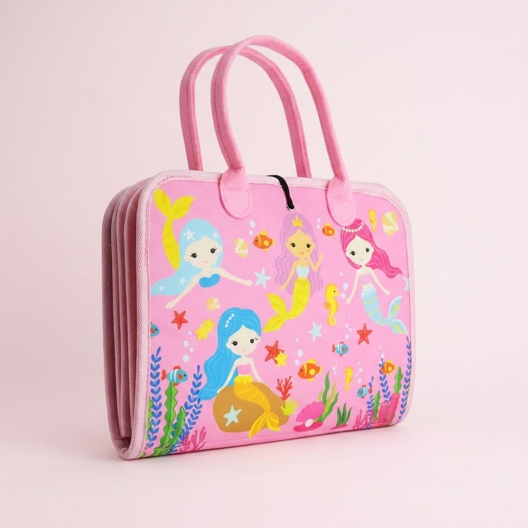 A folded pink fabric busy board with carry handles and colourful mermaid and sea creature illustrations stands against a pale pink background.