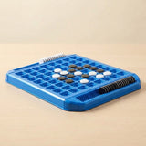 Blue plastic reversi game viewed from a low diagonal angle on pale wood, with black and white discs and edge storage slots.