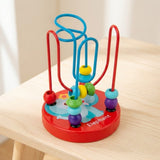 Wooden bead maze learning toy with turquoise and red wires and colorful beads stands on a light wooden stool against a cream background.