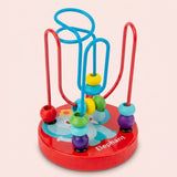 A wooden bead maze learning toy has colorful beads, red and blue tracks, and a red elephant-decorated base against a pale pink background.