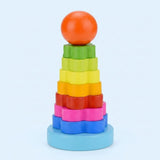 A wooden flower stacking learning toy has rainbow pieces, an orange ball top, and a light blue base against a pale blue background.