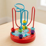 Wooden bead maze learning toy with colorful beads and a red elephant base sits on a pale wooden table beside a window.