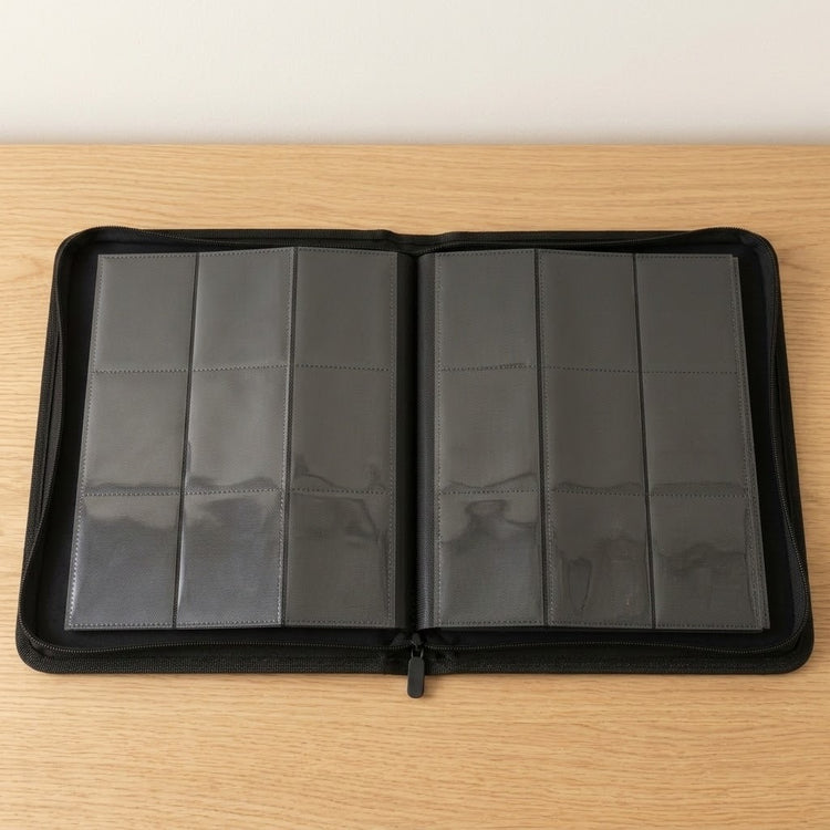 An open black zippered trading card binder displays two empty nine-pocket pages on a wooden tabletop against a cream wall.