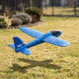 Blue speckled foam glider option for an airplane launcher toy, shown airborne above a sunlit lawn with a black cockpit.