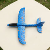 Blue foam glider for an airplane launcher toy has orange speckles and a black cockpit, resting on a white outdoor table.